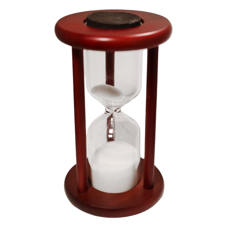 K&ouml;nnte beinhalten: Eine Sanduhr aus Holz mit einem roten Sockel und einer durchsichtigen Glasbirne, die mit wei&szlig;em Sand gef&uuml;llt ist. Die Sanduhr ist ein dekoratives Objekt, das zum Messen der Zeit verwendet werden kann.