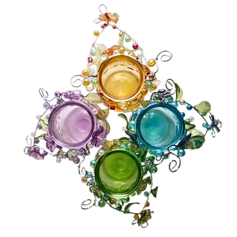 Pu&ograve; includere: Un portacandele decorativo con quattro bicchieri di vetro colorati in giallo, viola, turchese e verde. I bicchieri sono circondati da una cornice in filo d'argento con accenti floreali e perlati. Il portacandele &egrave; a forma di stella.