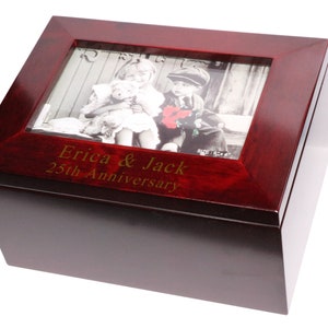 May include: A red wooden keepsake box with a photo frame on the lid. The frame contains a black and white photo of a young girl and boy. The box is engraved with the text "Erica & Jack 25th Anniversary".