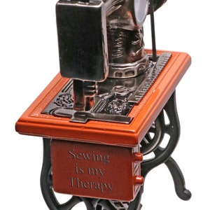 Peut inclure: Une petite figurine de machine &agrave; coudre rouge et noire avec les mots "Sewing is my Therapy" sur le devant.