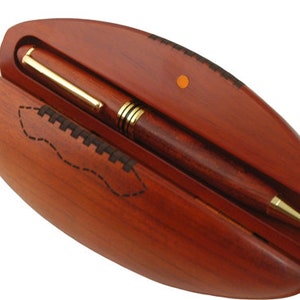 May include: A wooden pen case shaped like a football with a brown pen inside.