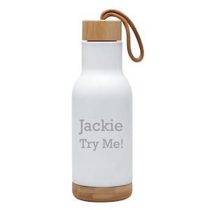 May include: White insulated water bottle with a bamboo lid and base, featuring a brown carrying strap. The bottle has the text "Jackie Try Me!" in gray. The bottle is designed to keep beverages cold or hot.
