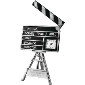 May include: A silver-colored clock shaped like a movie clapperboard with a black face and white numbers. The clock is on a tripod stand with a personalized inscription that reads "Julie & Matt Take Two".