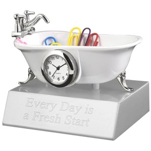 May include: White porcelain bathtub shaped desk organizer with a clock face and silver faucet. The bathtub has silver feet and is sitting on a silver base with the inscription "Every Day is a Fresh Start".