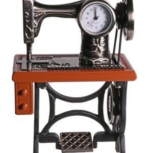 Peut inclure: Une horloge en forme de machine &agrave; coudre vintage avec un cadran noir et des aiguilles argent&eacute;es. L'horloge est mont&eacute;e sur un support en m&eacute;tal noir avec un dessus en bois brun. L'horloge est &agrave; quartz et est une pi&egrave;ce d&eacute;corative.