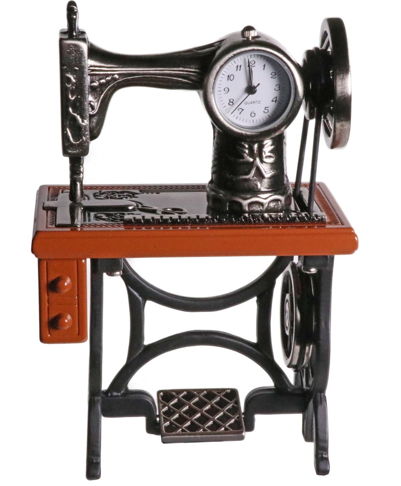 Peut inclure: Une horloge en forme de machine &agrave; coudre vintage avec un cadran noir et des aiguilles argent&eacute;es. L'horloge est mont&eacute;e sur un support en m&eacute;tal noir avec un dessus en bois brun. L'horloge est &agrave; quartz et est une pi&egrave;ce d&eacute;corative.