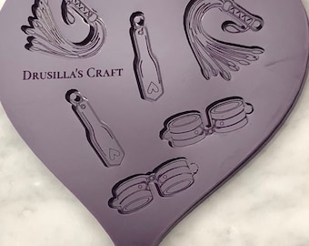 May include: Purple silicone mold in the shape of a heart with five different designs: a whip, a paddle, a pair of handcuffs, and two additional whips. The mold is labeled "Drusilla's Craft".
