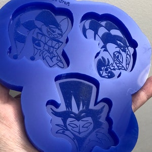May include: Blue silicone mold with three impressions of cartoon characters. The characters are a jester with a top hat, a jester with a crown, and a character with a top hat and a mustache. The mold is labeled "Brushie's Craft".