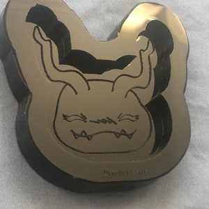 Op de afbeelding: Zwarte siliconen mal van een cartoonmonster met hoorns en een brede bek. De mal is hartvormig en heeft de tekst "Doodles Craft" aan de onderkant.