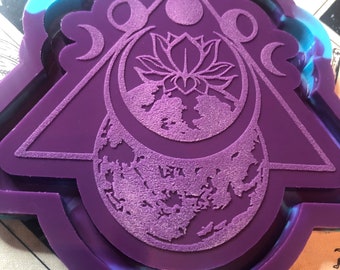 Puede incluir: Molde de silicona morado con un diseño de una luna creciente, una flor de loto y un globo terráqueo. El molde está rodeado por un borde azul y morado. El texto "Drusila's Craft" es visible en la parte inferior del molde.