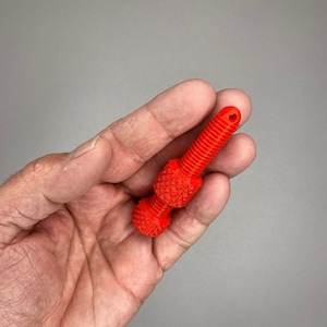 May include: Bright red, 3D-printed bottle stopper. The stopper features a threaded shaft, a textured diamond-patterned midsection, and a rounded, textured end. The stopper measures approximately 3.5 inches in length.