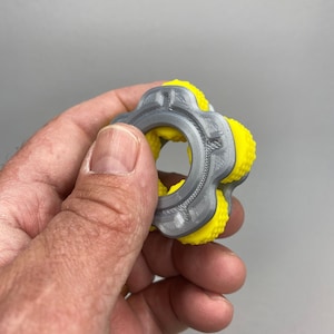 May include: A gray and yellow fidget toy with a textured surface and a ring in the center. The toy has five points with yellow bumps.