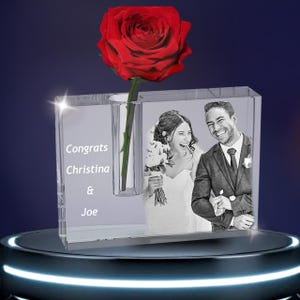 Può includere: Un vaso di cristallo trasparente con un'unica rosa rossa e una foto in bianco e nero di una sposa e uno sposo. Il vaso ha inciso il testo "Congrats Christina & Joe".