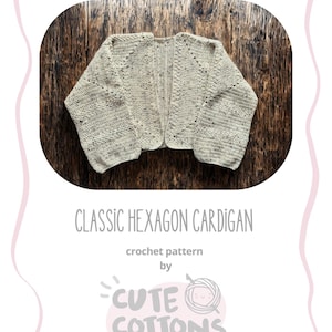 May include: A light beige Classic Hexagon Cardigan crochet pattern by Cute Cottons, displayed on a wooden surface. The open-fronted cardigan features a textured stitch. The image includes the text "CLASSIC HEXAGON CARDIGAN".