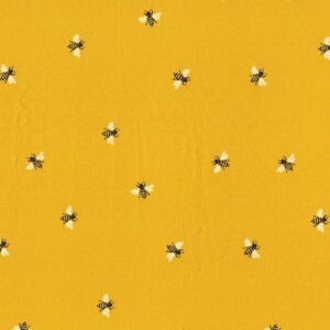 May include: A yellow fabric with a repeating pattern of black and white bees.