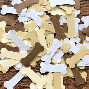 May include: A pile of brown, white, and beige paper bone shapes. The bones are scattered on a wooden surface.