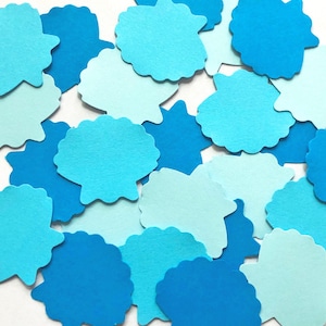 May include: A collection of blue and light blue paper cutouts in the shape of seashells. The cutouts are scattered on a white background.