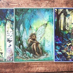 May include: Three rectangular art prints by Eneloj Designs featuring detailed illustrations of fairies in forest settings. The left print shows a fairy on a rock, the center shows a fairy among crystals, and the right shows a fairy with large wings.