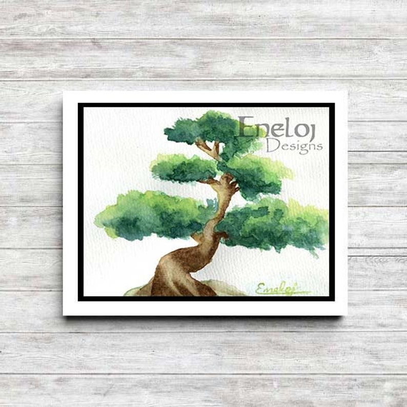 Puede incluir: Pintura acuarela de un &aacute;rbol bons&aacute;i con un tronco grueso y hojas verdes. La pintura est&aacute; enmarcada en un marco blanco con un passe-partout negro. La firma del artista, "Enel&oslash;j Designs", est&aacute; en la esquina superior derecha de la pintura.