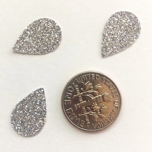 Op de afbeelding: Drie zilveren glitter-traanvormen, elk ongeveer zo groot als een Amerikaanse dime.