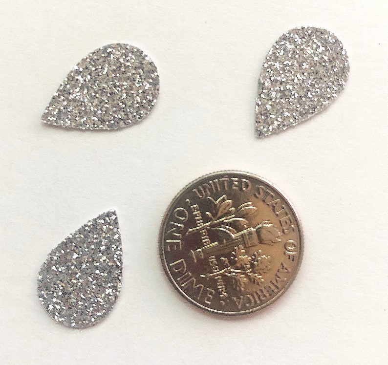 Op de afbeelding: Drie zilveren glitter-traanvormen, elk ongeveer zo groot als een Amerikaanse dime.