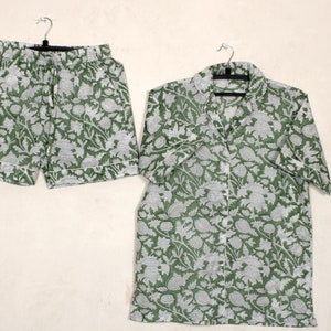 Può includere: Un pigiama verde e bianco a fantasia con una camicia a maniche corte e pantaloncini. La camicia ha una chiusura con bottoni sul davanti e i pantaloncini hanno una cintura elastica.