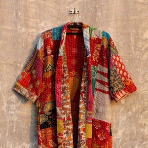 Puede incluir: Una larga bata roja acolchada de patchwork con estampado floral y geométrico. La bata tiene un cuello ancho y mangas tres cuartos.