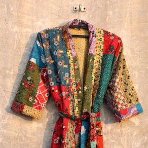 Könnte beinhalten: Eine bunte Patchwork-Robe mit langem, fließendem Design. Die Robe besteht aus verschiedenen Stoffen in Rot-, Blau-, Grün- und Gelbtönen. Sie hat einen traditionellen japanischen Kimono-Stil mit einem Bindegürtel.