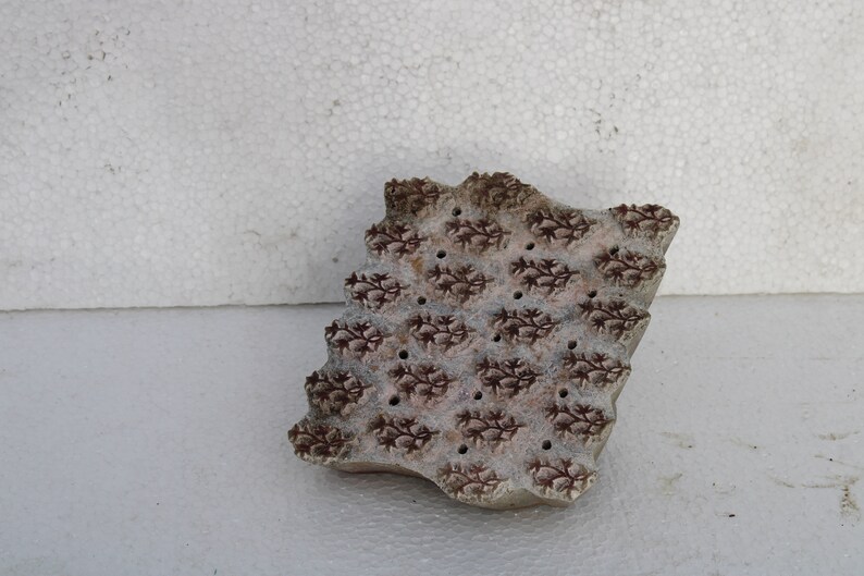 May include: A brown wooden block printing stamp with a repeating pattern of small floral designs. The stamp has a slightly irregular shape and is worn with age.