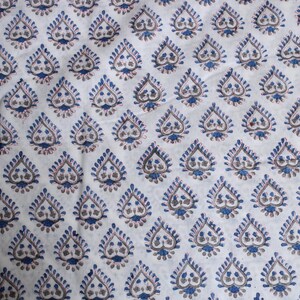 May include: White fabric featuring a repeating pattern of blue and brown teardrop-shaped designs. The teardrops have a detailed, stylized floral motif, creating a textured appearance. The fabric is likely cotton or a similar material.
