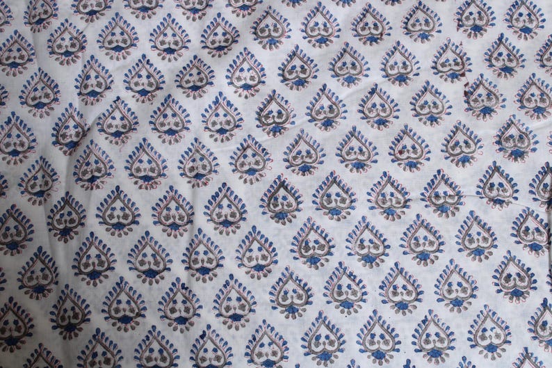 May include: White fabric featuring a repeating pattern of blue and brown teardrop-shaped designs. The teardrops have a detailed, stylized floral motif, creating a textured appearance. The fabric is likely cotton or a similar material.