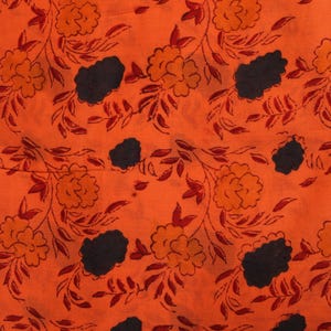 May include: Orange fabric with a repeating floral pattern. The design features orange and yellow flowers, dark blue cloud-like shapes, and red leaves and vines. The fabric has a textured appearance.