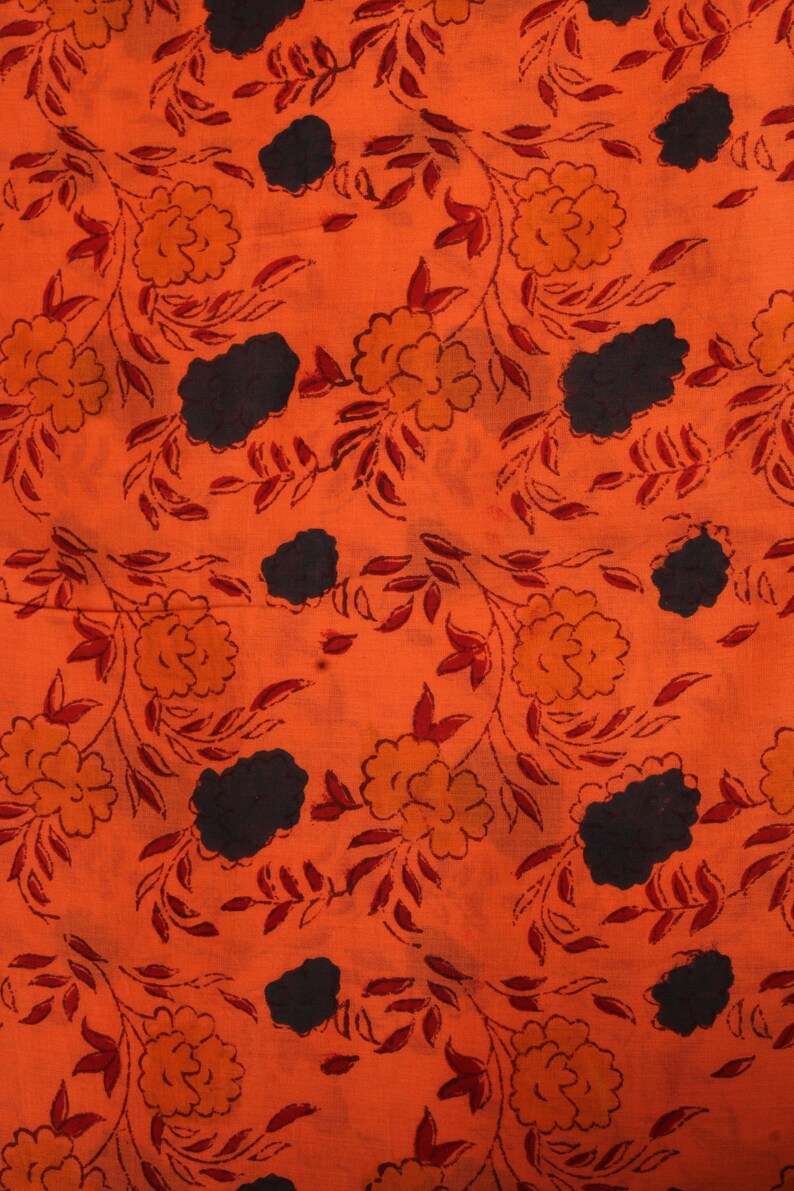May include: Orange fabric with a repeating floral pattern. The design features orange and yellow flowers, dark blue cloud-like shapes, and red leaves and vines. The fabric has a textured appearance.