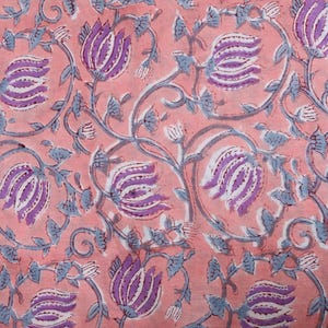 May include: Close-up of a fabric with a repeating floral pattern. The design features stylized purple and white flowers with blue-grey stems and leaves on a peach-coloured background. The pattern is detailed and intricate.
