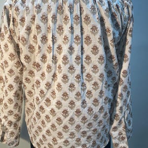 May include: A white shirt with a brown and green floral pattern. The long-sleeved shirt has a classic collar and cuffs. The floral design covers the entire shirt. The shirt is button-down.