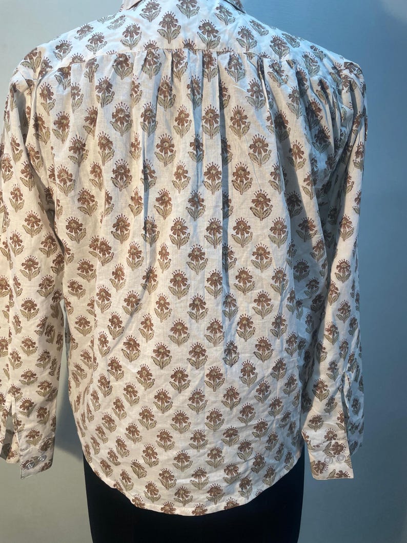 May include: A white shirt with a brown and green floral pattern. The long-sleeved shirt has a classic collar and cuffs. The floral design covers the entire shirt. The shirt is button-down.