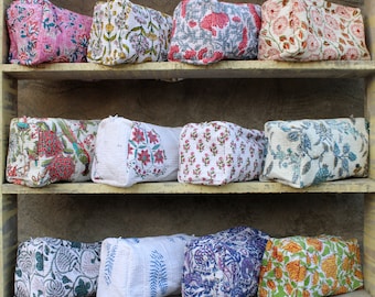 Pode incluir: Uma prateleira com 12 bolsas de tecido coloridas com padrões florais. As bolsas estão dispostas em três filas de quatro. As bolsas são feitas de um tecido macio acolchoado e têm um fecho de correr.