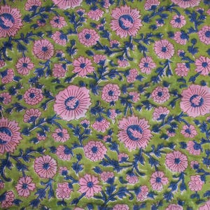 May include: A close-up of a fabric with a floral pattern. The design features pink flowers with blue centres and stems, set against a green background. The pattern is repeated across the fabric.