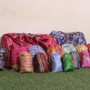 Puede incluir: Una colección de bolsas de cordón de colores hechas de tela con varios patrones. Las bolsas están dispuestas en una fila sobre una superficie verde.