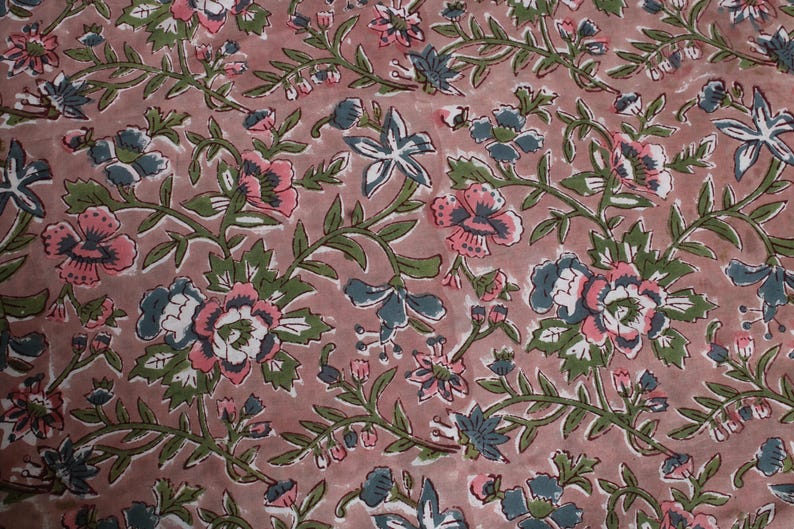 May include: A fabric featuring a floral pattern with pink, white, and blue flowers and green leaves on a dusty rose background. The design includes stylized blooms and winding vines, creating a classic, botanical aesthetic.