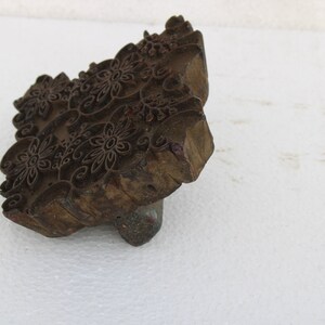 May include: A wooden printing block with a carved floral design. The block is brown and has a rough texture. It is used for creating patterns on fabric.