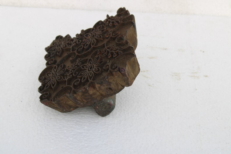 May include: A wooden printing block with a carved floral design. The block is brown and has a rough texture. It is used for creating patterns on fabric.