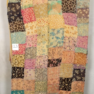 May include: A patchwork quilt featuring a mix of floral and geometric patterns in shades of pink, brown, blue, and green. The quilt is crafted from recycled saris and has a distinctive, vintage aesthetic.