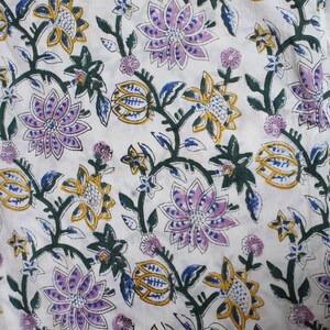 May include: White fabric with a floral pattern. The design features large, stylised flowers in shades of purple, yellow, and blue, connected by green vines and leaves. The overall aesthetic is reminiscent of a botanical print.