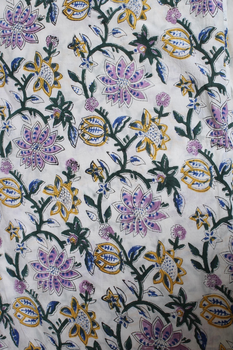 May include: White fabric with a floral pattern. The design features large, stylised flowers in shades of purple, yellow, and blue, connected by green vines and leaves. The overall aesthetic is reminiscent of a botanical print.