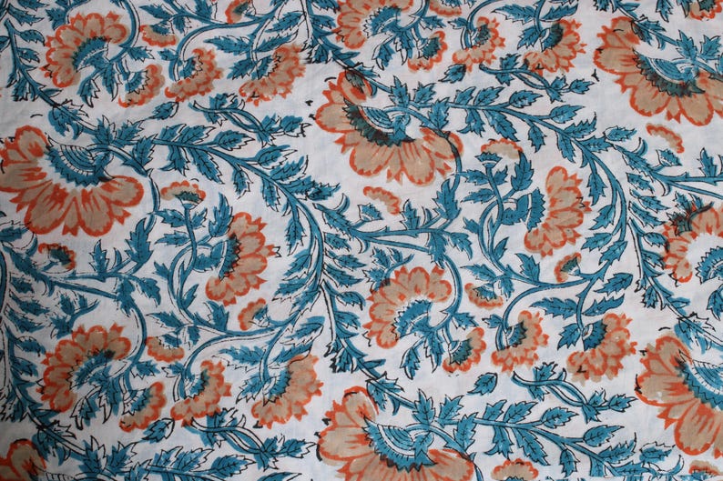 May include: White fabric with a repeating floral pattern. The design features large, stylized flowers in shades of peach and teal, with teal leaves and stems. The overall effect is a detailed, decorative textile.