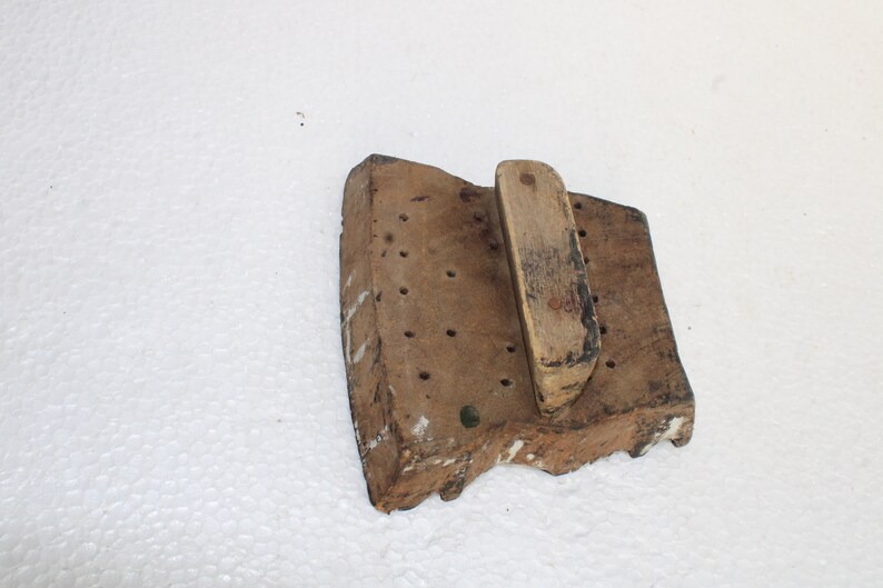 May include: A wooden printing block with a handle. The block has a rectangular shape and is covered in small holes. The handle is made of wood and is attached to the block.