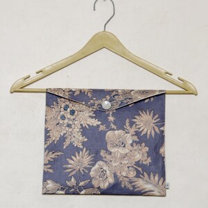 以下が含まれることがあります： ボタン留めの花柄の布製ポーチ。ポーチは木製ハンガーにかけられています。
