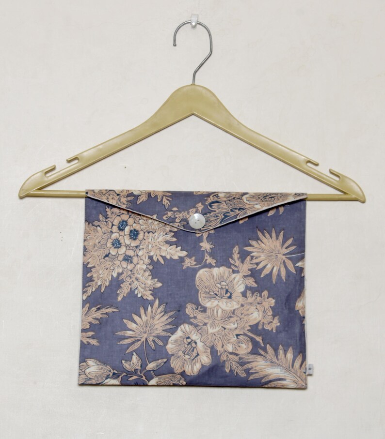 以下が含まれることがあります： ボタン留めの花柄の布製ポーチ。ポーチは木製ハンガーにかけられています。