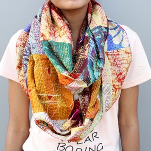 Puede incluir: Bufanda infinita de patchwork colorida con una variedad de patrones y colores, incluyendo naranja, amarillo, azul y rojo. La bufanda está hecha de una tela suave y ligera y se usa alrededor del cuello.